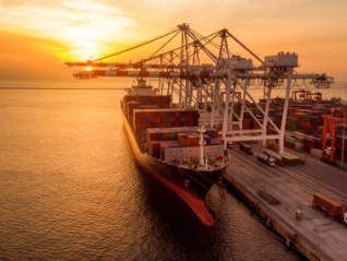 Crane loading container onto container ship at sunset