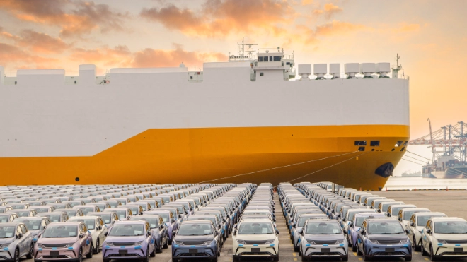new cars parked in front of a ship in the harbour